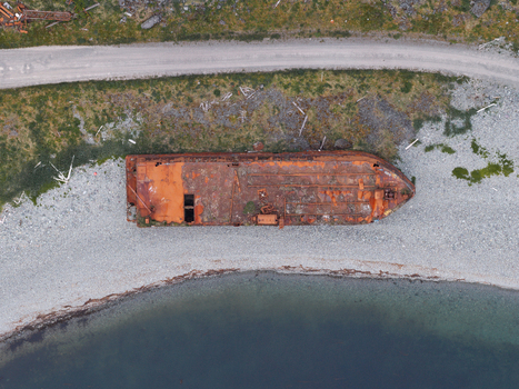 Aerial view of a rusted shipwreck resting on a rocky beach near the shoreline in Unalaska Alaska United States.