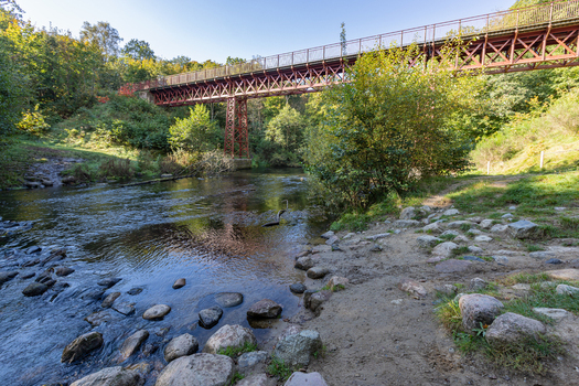 View of The Uncovered Bridge spanning the Gudena river surrounded by lush green trees and rocky riverbanks in Braedstrup Jutland Denmark. View of The Uncovered Bridge spanning the Gudena river surrounded by lush green trees and rocky riverbanks in Braedstrup Jutland Denmark.