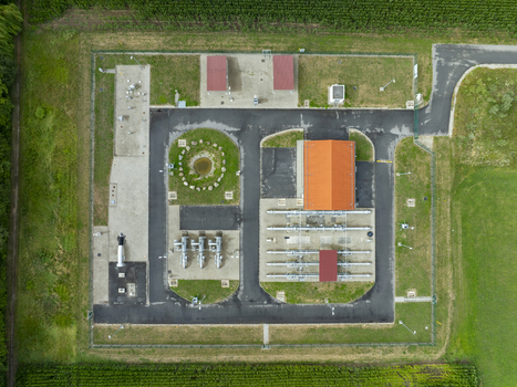 Aerial view of a gas pressure regulating station with industrial piping paved access paths and a building with an orange roof surrounded by green fields in Finsing Bavaria Germany.