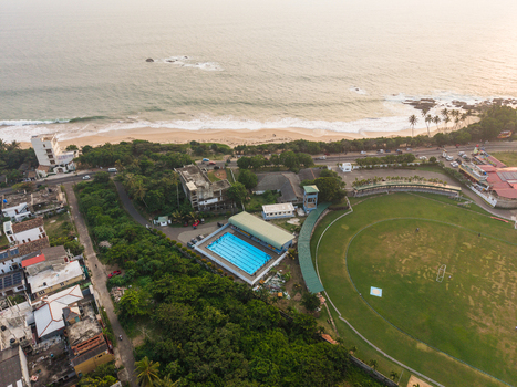 Aerial view of a cricket field and a blue swimming pool near the sandy coastline with waves crashing on the shore Galle Southern Province Sri Lanka.