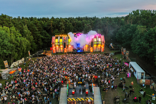 Herzogenaurach Germany 24 July 2025 Aerial view of the Open Beatz Festival stage with a large crowd of people dancing and smoke effects surrounded by a dense forest.