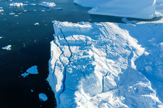 Aerial view of the massive Ilulissat glacier iceberg with deep crevasses floating in the dark blue waters of Greenland. Aerial view of the massive Ilulissat glacier iceberg with deep crevasses floating in the dark blue waters of Greenland.