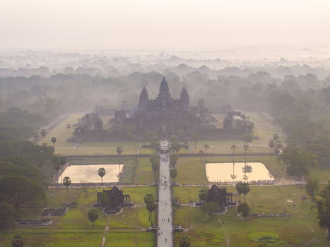 Aerial view of the ancient Angkor Wat temple complex shrouded in morning mist with its iconic stone towers and surrounding lush forest in Krong Siem Reap Siem Reap Province Cambodia. Aerial view of the ancient Angkor Wat temple complex shrouded in morning mist with its iconic stone towers and surrounding lush forest in Krong Siem Reap Siem Reap Province Cambodia.