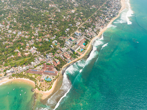 Aerial view of the tropical coastline featuring turquoise ocean waves sandy beaches and dense green vegetation surrounding coastal buildings in Hikkaduwa Southern Province Sri Lanka. Aerial view of the tropical coastline featuring turquoise ocean waves sandy beaches and dense green vegetation surrounding coastal buildings in Hikkaduwa Southern Province Sri Lanka.