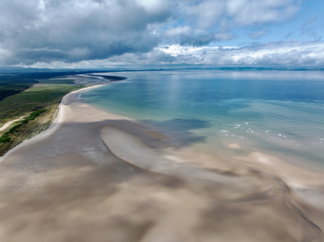 Aerial view of the Moray Firth Coast featuring expansive sandy beaches tidal flats and calm waters under a cloudy sky in Nairn Scotland United Kingdom.