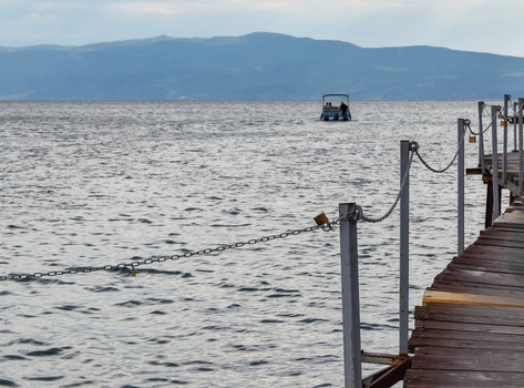View of a wooden pier extending into the calm waters of Lake Ohrid with a small boat in the distance and mountains in Ohrid Municipality of Ohrid North Macedonia. View of a wooden pier extending into the calm waters of Lake Ohrid with a small boat in the distance and mountains in Ohrid Municipality of Ohrid North Macedonia.