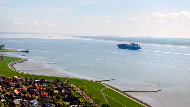 Brunsbuttel Schleswig Holstein Germany 30 May 2025 Aerial view of a large container ship navigating the Elbe river near the green dikes and residential houses of Brunsbuttel. Brunsbuttel Schleswig Holstein Germany 30 May 2025 Aerial view of a large container ship navigating the Elbe river near the green dikes and residential houses of Brunsbuttel.