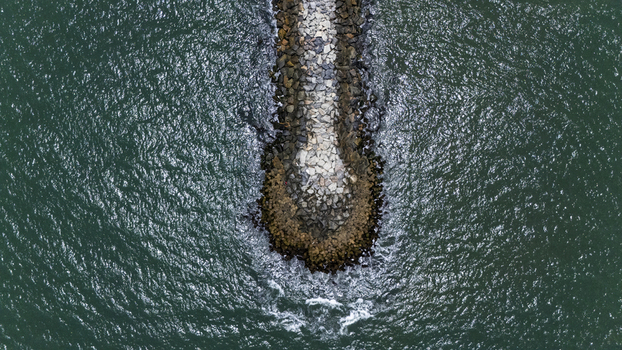 Aerial view of a stone breakwater extending into the turquoise ocean water with small waves Lekki Lagos Nigeria. Aerial view of a stone breakwater extending into the turquoise ocean water with small waves Lekki Lagos Nigeria.