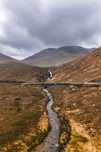 Aerial view of Eas a Bhradain waterfall flowing through the rugged moorland landscape with mountains under a cloudy sky Isle of Skye Scotland United Kingdom. Aerial view of Eas a Bhradain waterfall flowing through the rugged moorland landscape with mountains under a cloudy sky Isle of Skye Scotland United Kingdom.