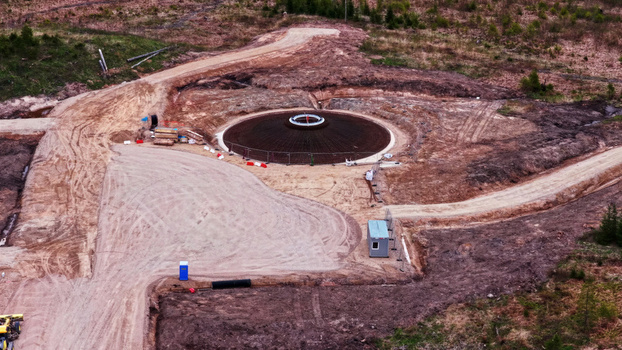 Aerial view of a wind turbine foundation under construction in a rural area with dirt access roads and site equipment in Latvia. Aerial view of a wind turbine foundation under construction in a rural area with dirt access roads and site equipment in Latvia.