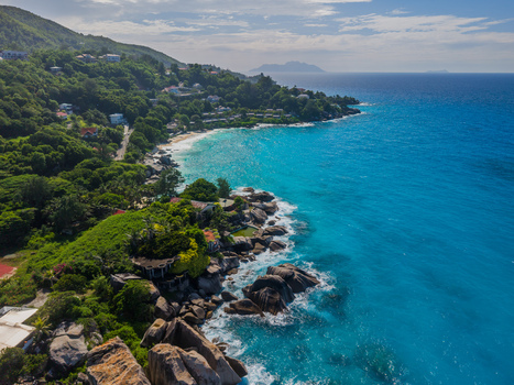 Aerial view of turquoise waters meeting the lush green coastline near granite boulders with buildings nestled among the trees La Retraite Mahe Island Seychelles. Aerial view of turquoise waters meeting the lush green coastline near granite boulders with buildings nestled among the trees La Retraite Mahe Island Seychelles.