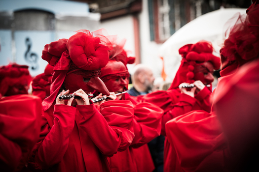 Basel Switzerland 10 March 2025 View of vibrant red clad figures masked and playing flutes during Fasnacht a burst of color against the muted urban backdrop. Basel Switzerland 10 March 2025 View of vibrant red clad figures masked and playing flutes during Fasnacht a burst of color against the muted urban backdrop.