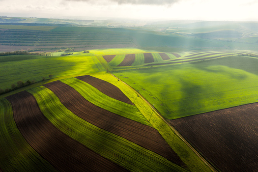 Aerial view of rolling green hills and striped agricultural fields under dramatic sunlight and cloud shadows in Klobouky u Brna Jihomoravsky kraj Czechia. Aerial view of rolling green hills and striped agricultural fields under dramatic sunlight and cloud shadows in Klobouky u Brna Jihomoravsky kraj Czechia.