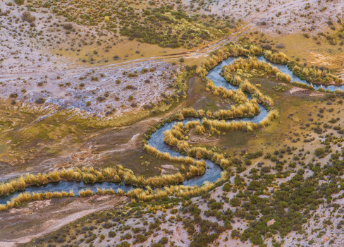 Aerial view of the winding river flowing through the arid landscape of Canon de Alota surrounded by golden grasses and rocky terrain in Villa Alota Departamento de Potosi Bolivia. Aerial view of the winding river flowing through the arid landscape of Canon de Alota surrounded by golden grasses and rocky terrain in Villa Alota Departamento de Potosi Bolivia.