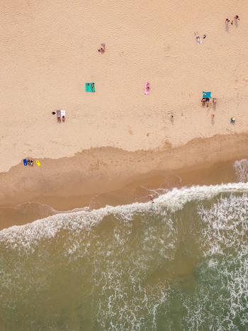 Aerial view of a sandy beach with people relaxing on colorful towels and umbrellas near the gentle surf of the ocean in Vietnam. Aerial view of a sandy beach with people relaxing on colorful towels and umbrellas near the gentle surf of the ocean in Vietnam.