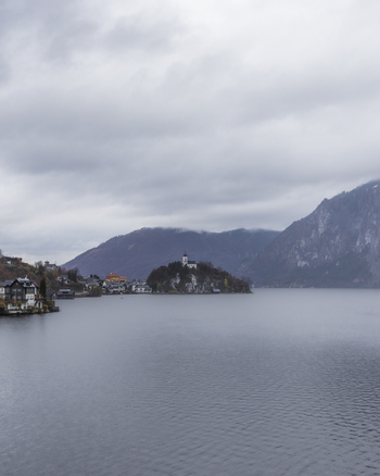 View of the historic village of Hallstatt with its iconic church on the lakefront under a cloudy sky and misty mountains Hallstatt Upper Austria Austria. View of the historic village of Hallstatt with its iconic church on the lakefront under a cloudy sky and misty mountains Hallstatt Upper Austria Austria.