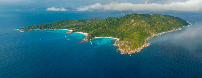 Aerial view of the lush green landscape of Anse Reunion island surrounded by turquoise waters white sandy beaches and boats in the Indian Ocean Anse Reunion La Digue Seychelles.