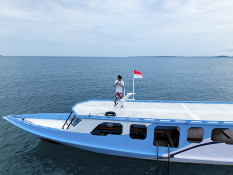 Aerial view of a person standing on a white and blue boat with an Indonesian flag waving gently on the serene ocean Karimunjawa Central Java Indonesia.