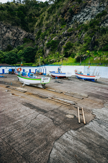 View of vibrant fishing boats resting on a cracked concrete platform against a backdrop of lush green cliffs a serene coastal scene Caloura A&ccedil;ores Portugal.