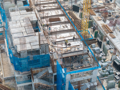 Bukit Tambun Malaysia 25 September 2026 Aerial view of a busy construction site with workers in hard hats a yellow crane concrete structures and blue safety netting. Bukit Tambun Malaysia 25 September 2026 Aerial view of a busy construction site with workers in hard hats a yellow crane concrete structures and blue safety netting.