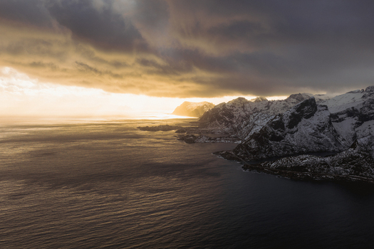 Aerial view of the dramatic coastline meeting the moody waters under an evocative sky Reinebringen Nordland Norway.