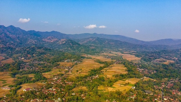 Aerial view of the rural landscape of Ngadiharjo featuring terraced rice fields small village houses and lush vegetation nestled among mountains in Borobudur Central Java Indonesia.