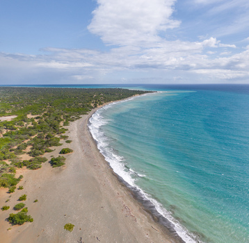 Aerial view of Las Calderas coastline with turquoise waters sandy beach and lush green vegetation under a blue sky in Bani Peravia Dominican Republic.