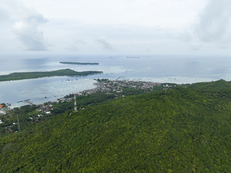 Aerial view of lush green hills cascading towards the coastal town where the sea meets the land in a vibrant display of nature s beauty Karimunjawa Central Java Indonesia.