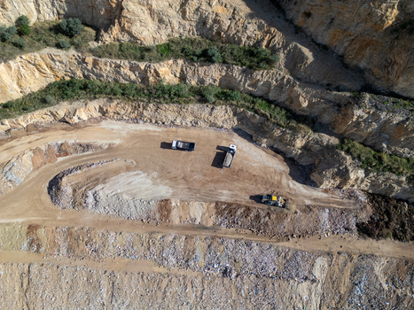 Aerial view of a quarry in Teulada with heavy machinery including trucks and an excavator operating on a dirt floor surrounded by rocky cliff faces in Teulada Valencian Community Spain.