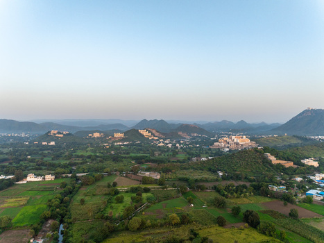 Aerial view of historic palaces nestled among rolling hills and lush green fields in Udaipur Rajasthan India.