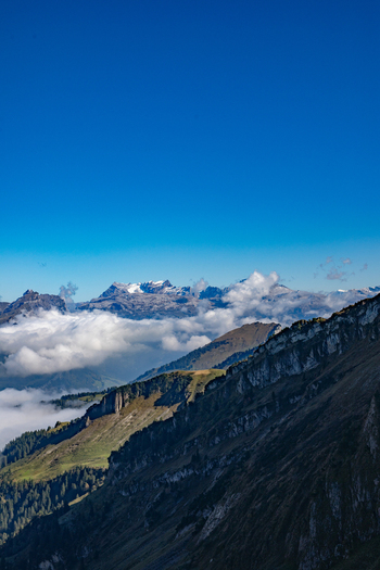 Aerial view of the Swiss Alps with snow capped peaks rolling green slopes and a sea of clouds under a clear blue sky in Airolo Ticino Switzerland. Aerial view of the Swiss Alps with snow capped peaks rolling green slopes and a sea of clouds under a clear blue sky in Airolo Ticino Switzerland.