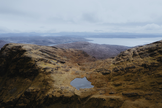 Aerial view of Bla Bheinn with a small mountain tarn nestled in the rugged rocky terrain under a cloudy sky in the Isle of Skye Scotland United Kingdom. Aerial view of Bla Bheinn with a small mountain tarn nestled in the rugged rocky terrain under a cloudy sky in the Isle of Skye Scotland United Kingdom.