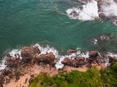 Aerial view of Gintota beach with turquoise ocean waves crashing against dark rocky formations and lush tropical palm trees in Galle Southern Province Sri Lanka. Aerial view of Gintota beach with turquoise ocean waves crashing against dark rocky formations and lush tropical palm trees in Galle Southern Province Sri Lanka.