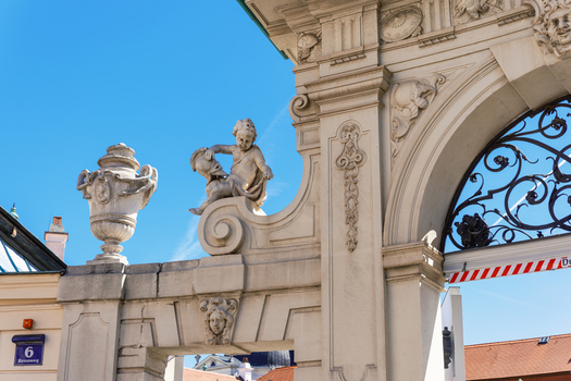View of the ornate stone sculptures and decorative archway at the entrance of the Belvedere Palace under a clear blue sky in Vienna Austria. View of the ornate stone sculptures and decorative archway at the entrance of the Belvedere Palace under a clear blue sky in Vienna Austria.