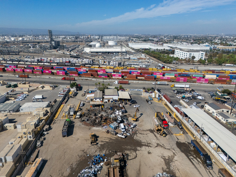 Aerial view of an industrial scrap yard and rail yard with colorful shipping containers heavy machinery and warehouses in Carson California United States.