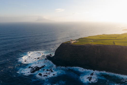 Aerial view of Farol de Albarnaz on a steep cliff surrounded by green fields and the Atlantic Ocean in Ponta Delgada Acores Portugal. Aerial view of Farol de Albarnaz on a steep cliff surrounded by green fields and the Atlantic Ocean in Ponta Delgada Acores Portugal.