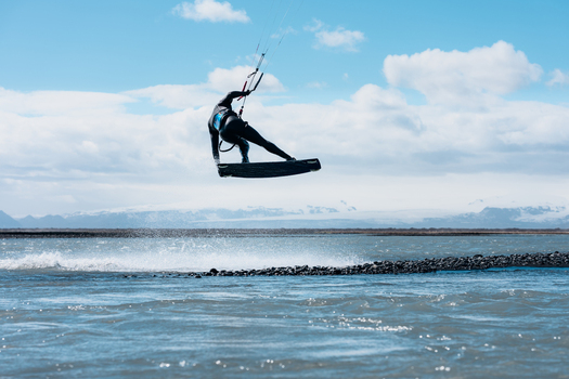 View of a kitesurfer performing a jump over the water with snow capped mountains in the background in Skaftarhreppur Iceland.