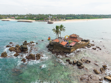 Aerial view of Seenigama Muhudu Dewalaya temple on a rocky island surrounded by turquoise ocean water and palm fringed coastline Peraliya Sri Lanka. Aerial view of Seenigama Muhudu Dewalaya temple on a rocky island surrounded by turquoise ocean water and palm fringed coastline Peraliya Sri Lanka.
