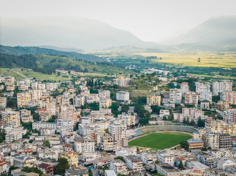 Aerial view of the urban landscape with residential buildings and a green sports stadium nestled against rolling hills and mountains in Gjirokaster Gjirokaster County Albania. Aerial view of the urban landscape with residential buildings and a green sports stadium nestled against rolling hills and mountains in Gjirokaster Gjirokaster County Albania.