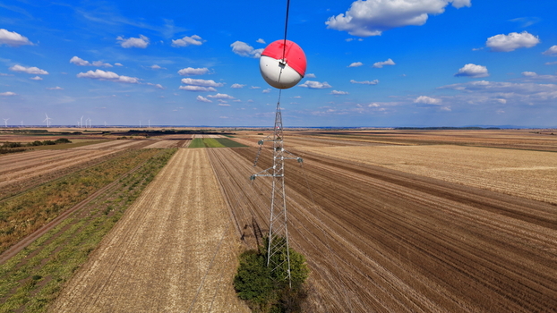 Aerial view of a high voltage transmission tower with a red and white marker ball on the power line set against a vast agricultural landscape in Bavaniste Vojvodina Serbia. Aerial view of a high voltage transmission tower with a red and white marker ball on the power line set against a vast agricultural landscape in Bavaniste Vojvodina Serbia.