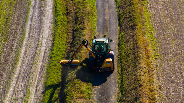 Aerial view of a tractor with a hedge trimmer attachment working on a rural path at Pepperbox Hill in Salisbury England United Kingdom. Aerial view of a tractor with a hedge trimmer attachment working on a rural path at Pepperbox Hill in Salisbury England United Kingdom.
