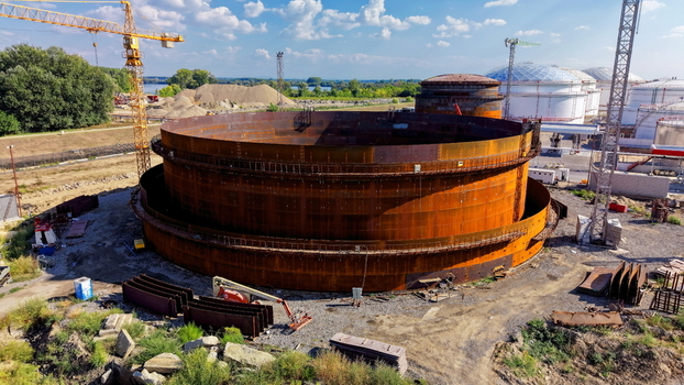 Aerial view of the assembly of a large refinery oil storage tank under construction featuring rusted steel panels construction cranes and industrial equipment in Kovin Vojvodina Serbia. Aerial view of the assembly of a large refinery oil storage tank under construction featuring rusted steel panels construction cranes and industrial equipment in Kovin Vojvodina Serbia.