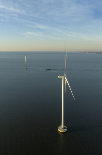 Aerial view of offshore wind turbines standing in calm blue water with a small boat in the distance under a clear sky in Netherlands. Aerial view of offshore wind turbines standing in calm blue water with a small boat in the distance under a clear sky in Netherlands.
