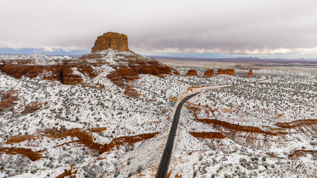 Aerial view of a majestic red rock mesa covered in fresh snow with a winding road through the desert landscape in Page Arizona United States.