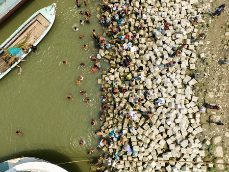 Aerial view of people swimming in murky green waters beside a rocky shoreline dotted with boats creating a vibrant contrast of life and landscape Charmonai Barisal Division Bangladesh. Aerial view of people swimming in murky green waters beside a rocky shoreline dotted with boats creating a vibrant contrast of life and landscape Charmonai Barisal Division Bangladesh.