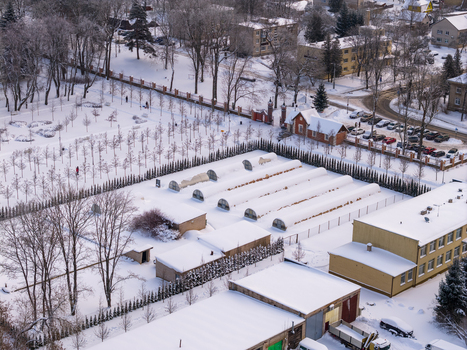 Aerial view of snow covered greenhouses and bare trees in a winter park landscape with residential buildings in Lithuania. Aerial view of snow covered greenhouses and bare trees in a winter park landscape with residential buildings in Lithuania.