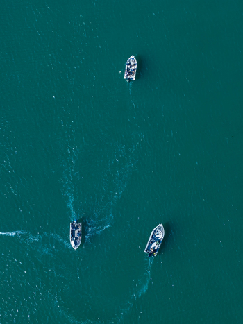 Aerial view of three salmon fishing boats navigating through deep blue water in Gold Beach Oregon United States.