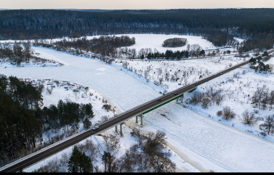 Aerial view of a bridge crossing a frozen river surrounded by snow covered fields and dense pine forests in Lithuania. Aerial view of a bridge crossing a frozen river surrounded by snow covered fields and dense pine forests in Lithuania.