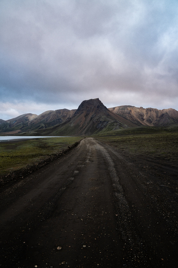View of a dark gravel road leading toward a mountain under a cloudy sky the Icelandic landscape a symphony of rugged beauty Rangárþing ytra Iceland. View of a dark gravel road leading toward a mountain under a cloudy sky the Icelandic landscape a symphony of rugged beauty Rangárþing ytra Iceland.