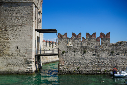 View of the historic Scaligero Castle with its stone walls and drawbridge over the turquoise water of Lake Garda in Sirmione Lombardy Italy.